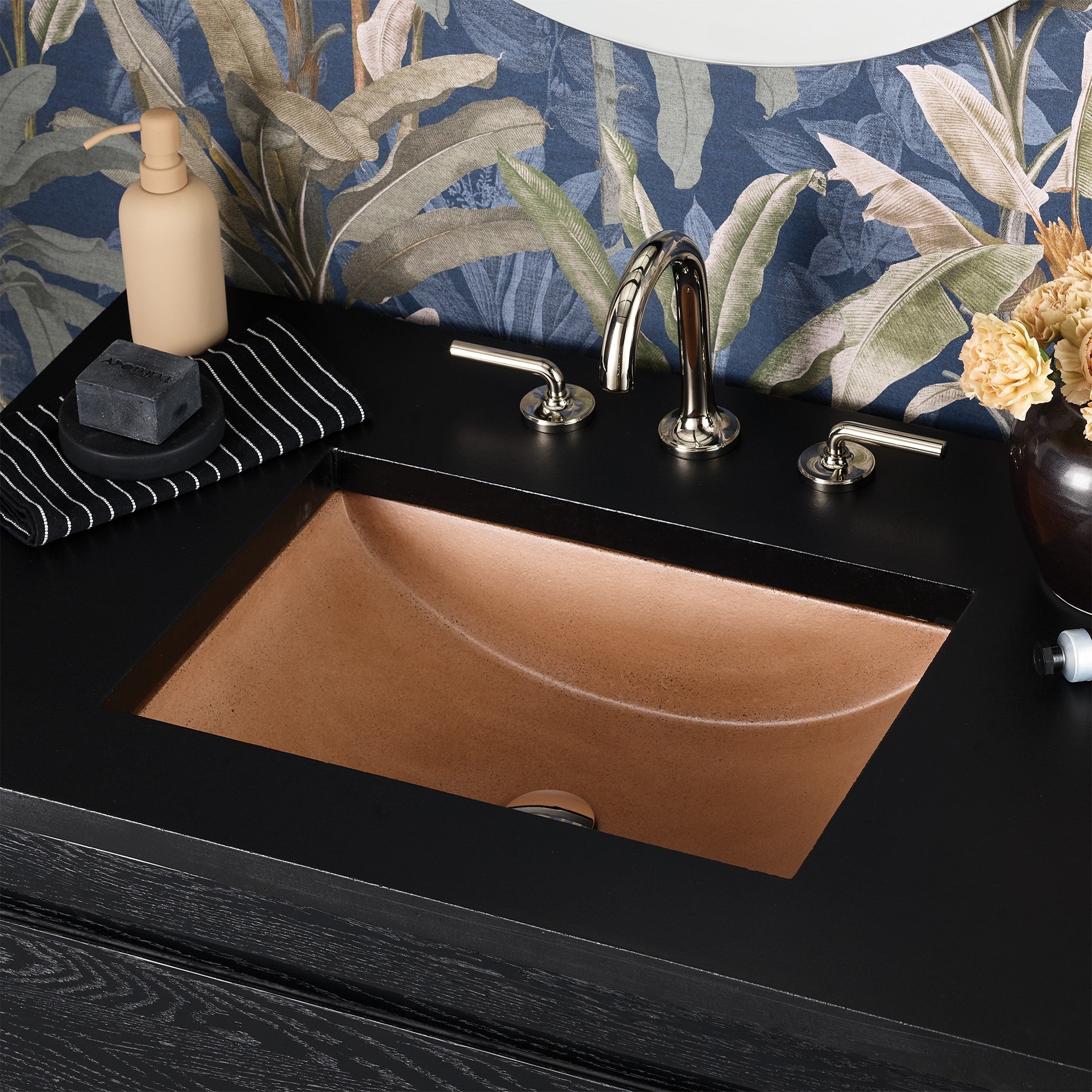 Terracotta rectangular undermount sink with curved basin set in black countertop, chrome faucet and accessories visible.