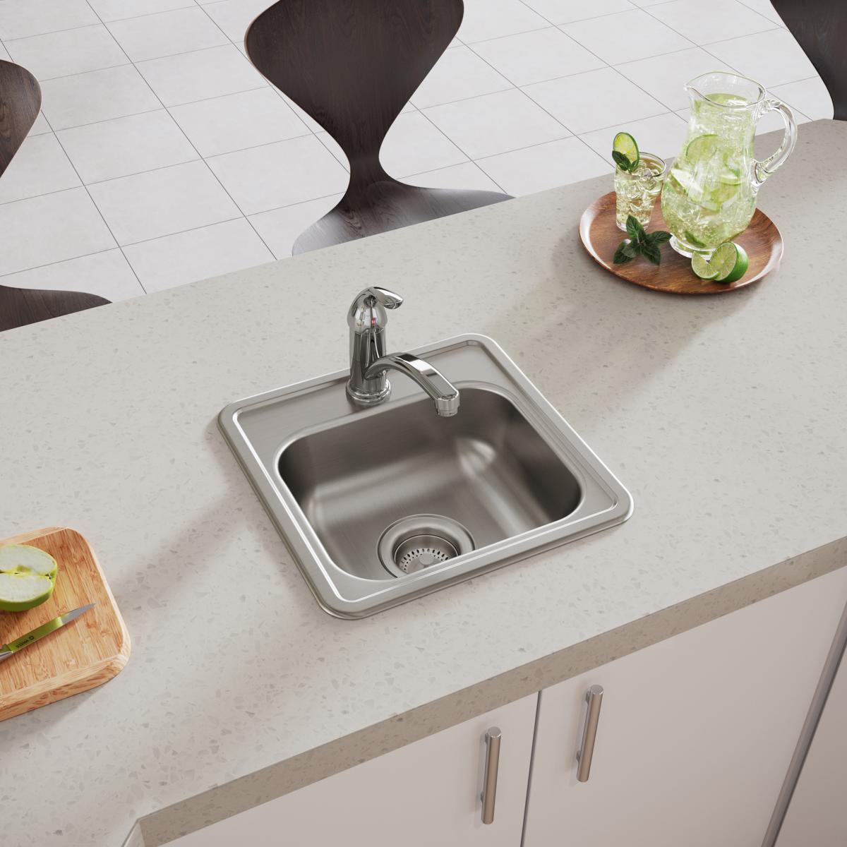 Stainless steel drop-in bar sink with single bowl, chrome faucet, and drain strainer installed in light countertop.