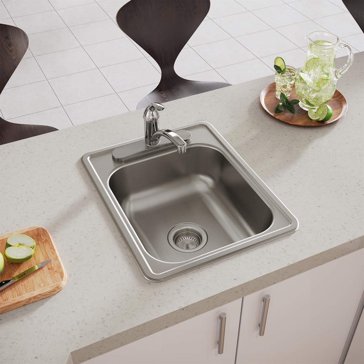 Stainless steel drop-in bar sink with single bowl, chrome faucet, and drain strainer installed in white countertop.
