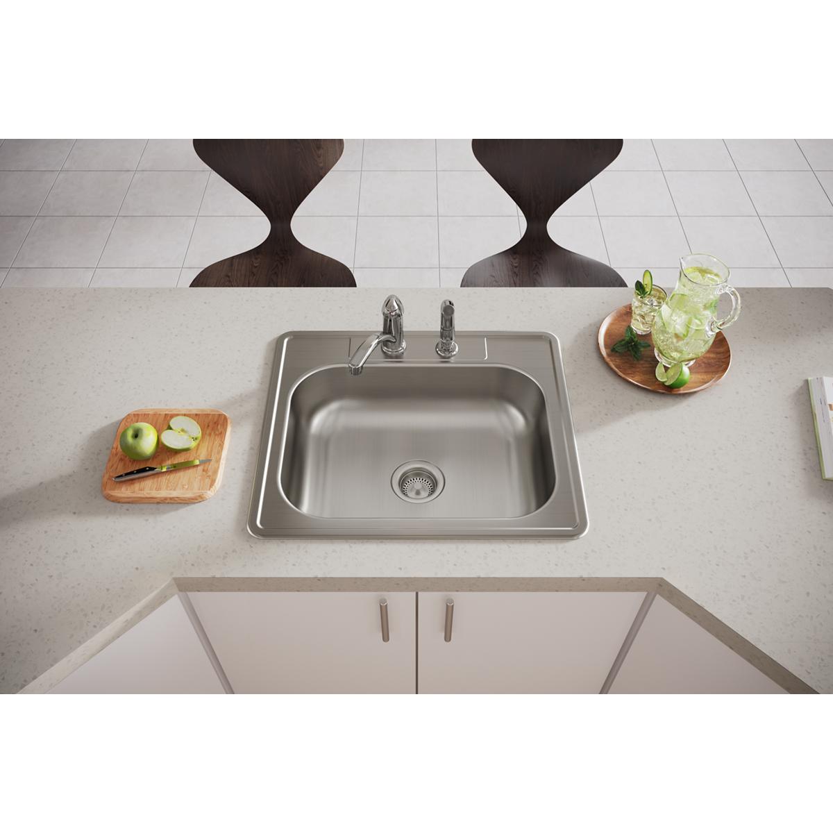 Stainless steel drop-in sink with single bowl and two faucet holes installed in light countertop with chrome faucet.