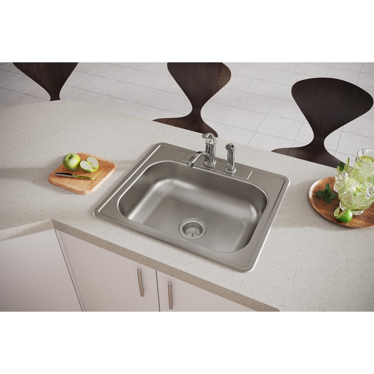 Stainless steel drop-in sink with single bowl and two faucet holes installed in countertop with chrome faucet.