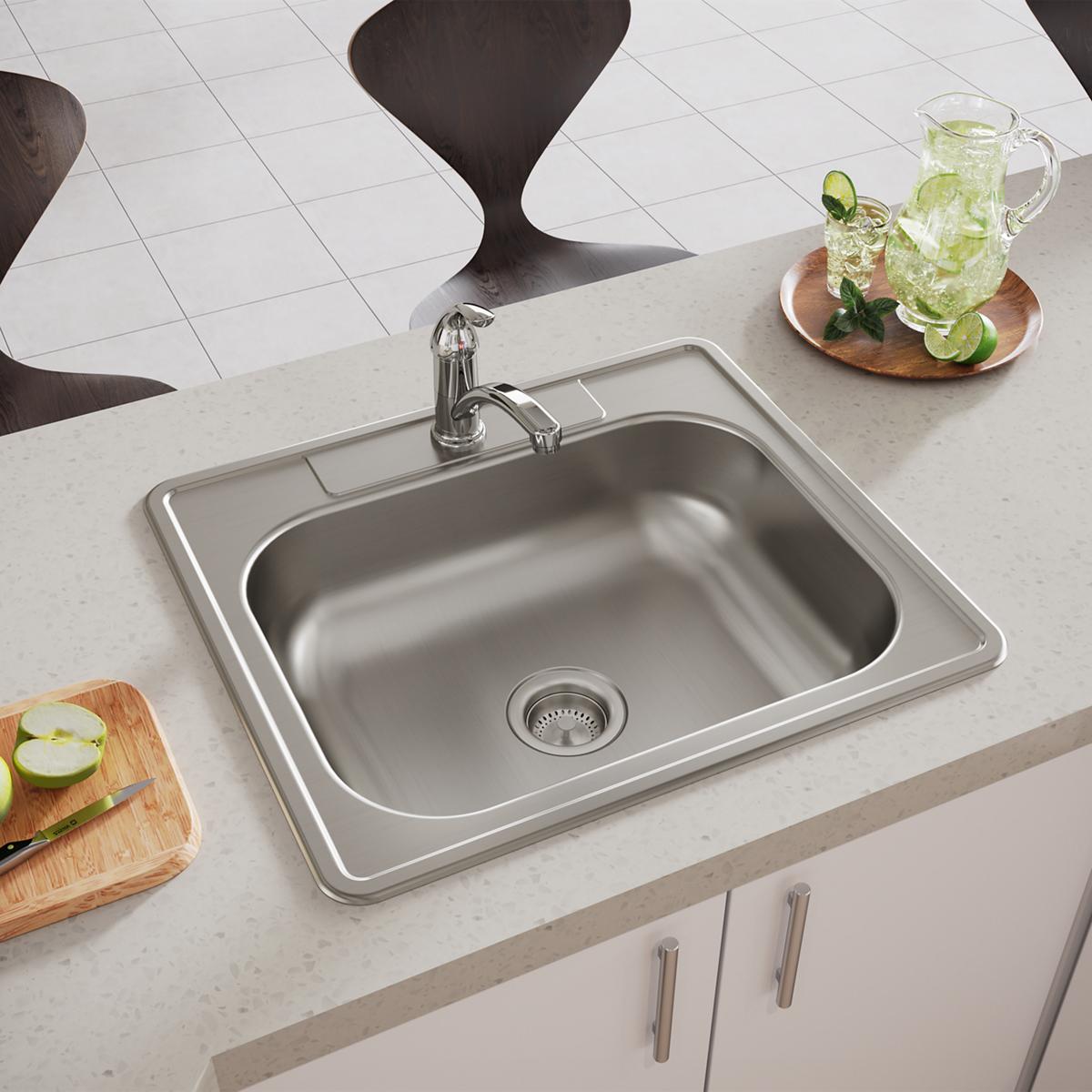Stainless steel single bowl drop-in sink with chrome faucet installed in white countertop next to cutting boards and beverage