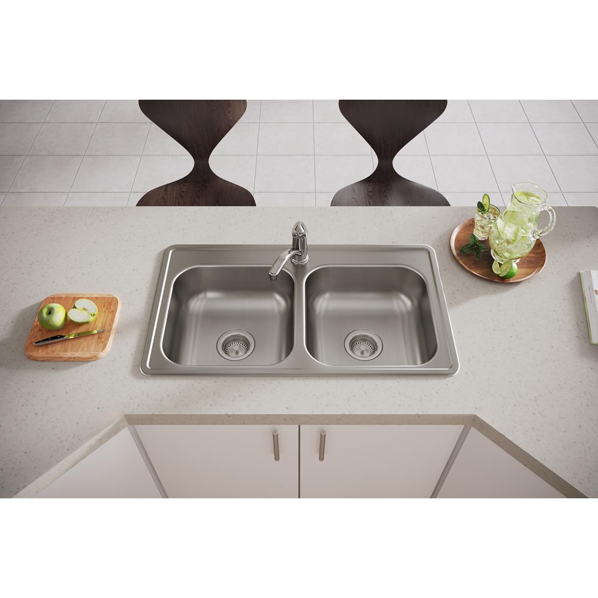 Stainless steel double bowl drop-in sink with single faucet hole installed in light countertop above white cabinetry.