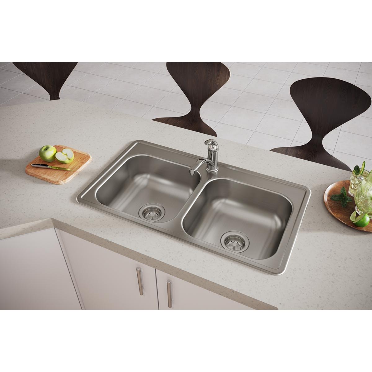 Stainless steel double bowl drop-in sink with faucet installed in white countertop next to kitchen cabinets.