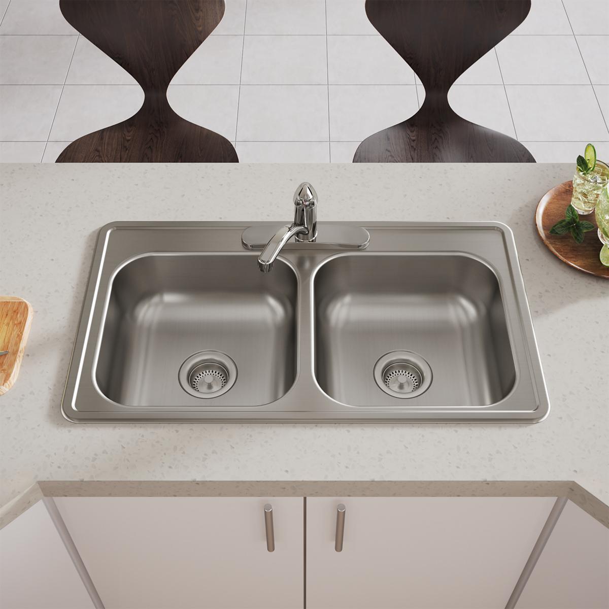 Stainless steel drop-in double bowl sink with three faucet holes and drain strainers installed in countertop.