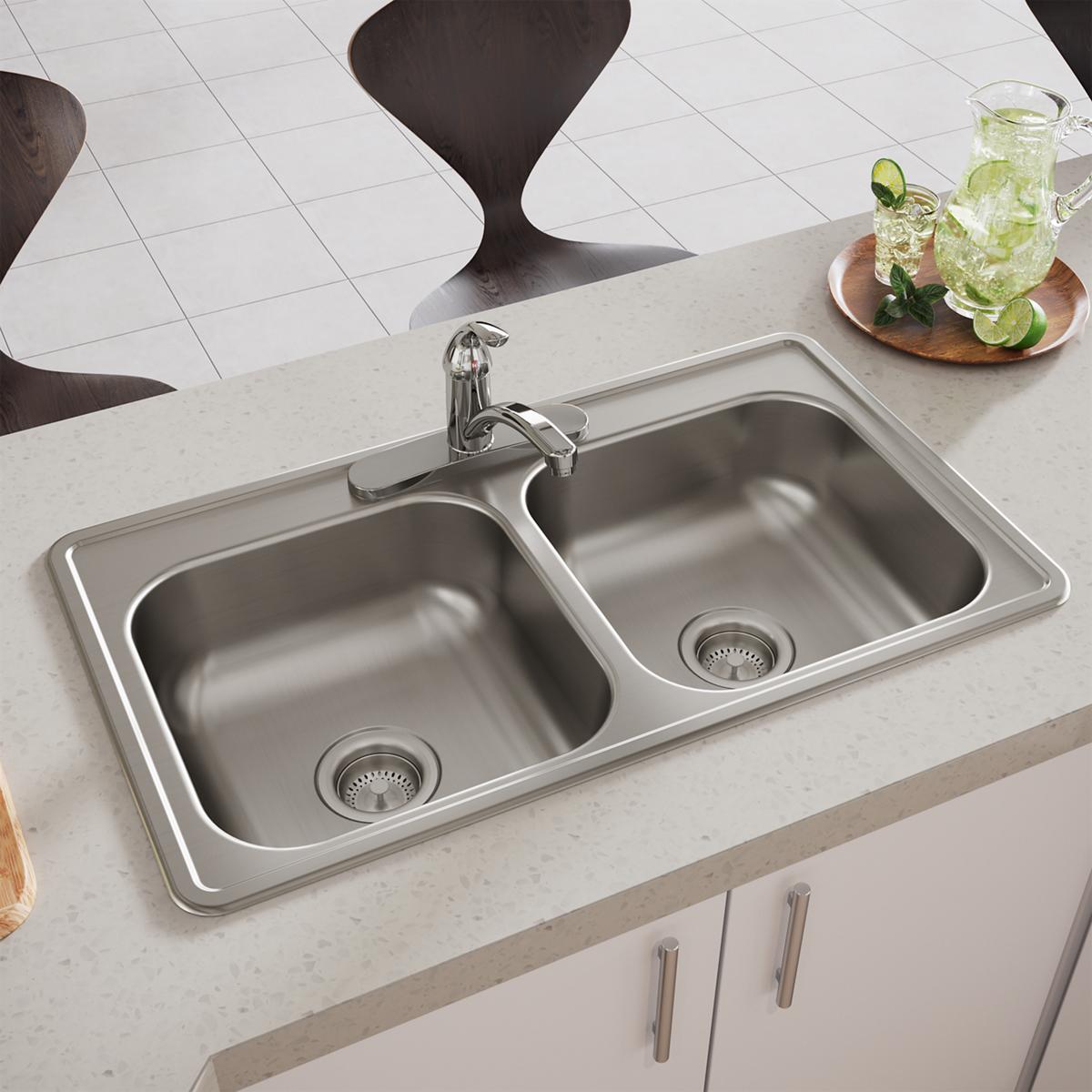 Stainless steel double bowl drop-in sink with two equal basins, drain strainers, and chrome faucet installed in light counter