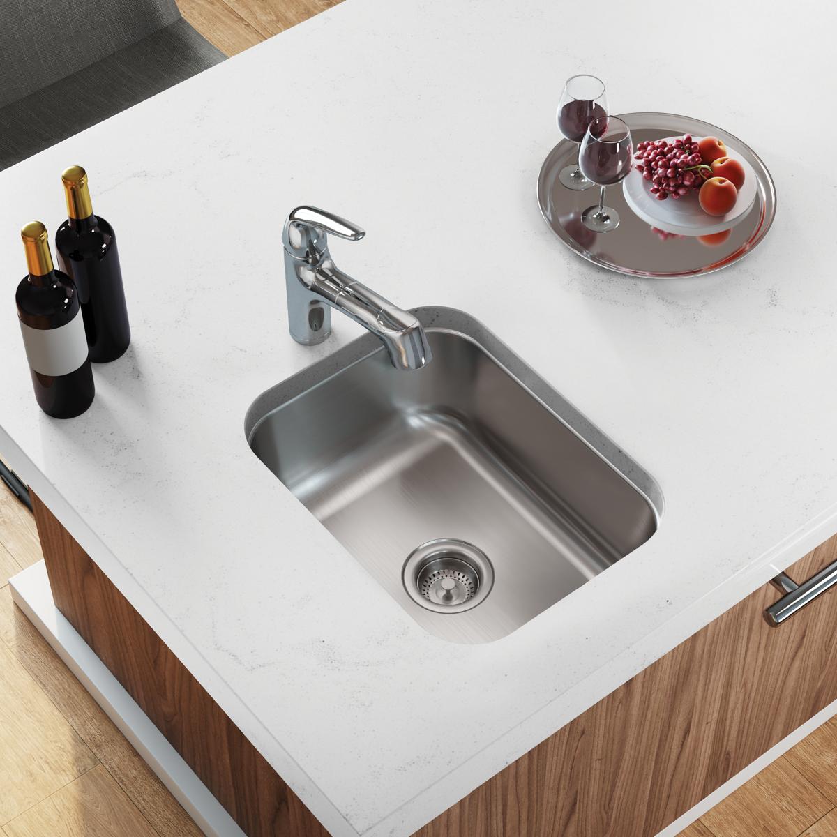 Stainless steel single bowl undermount sink installed in white countertop with chrome faucet and drain strainer.