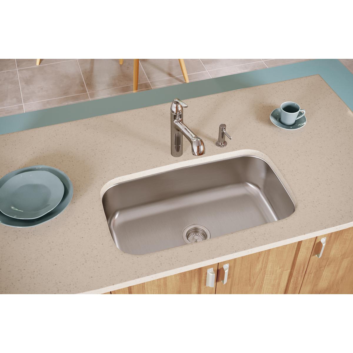 Stainless steel single bowl undermount sink installed in beige countertop with chrome faucet and wooden cabinet base.