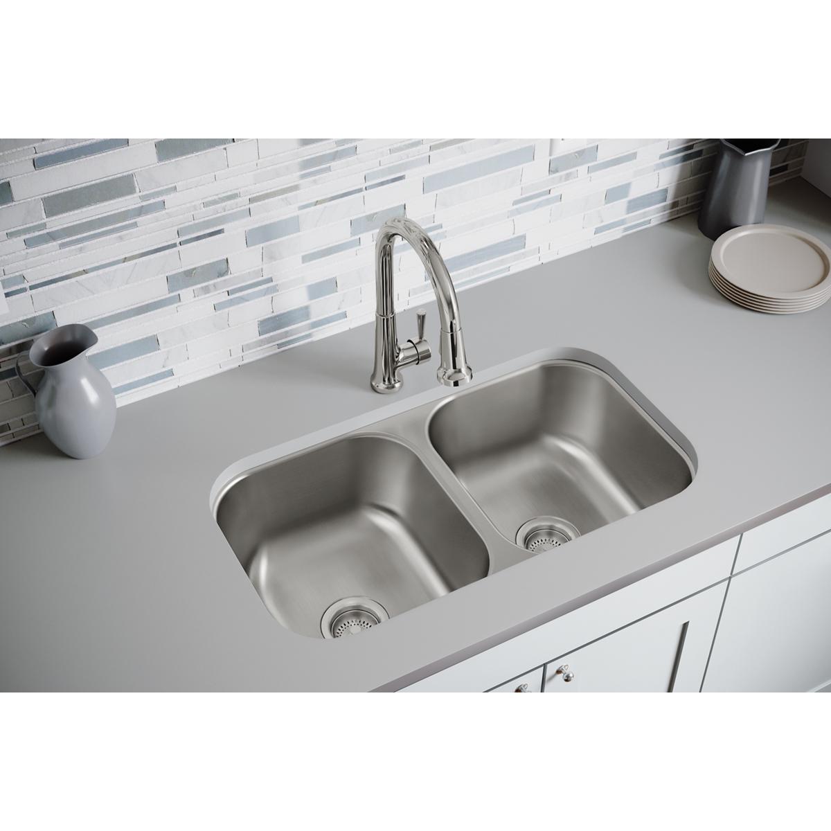 Stainless steel double bowl undermount sink installed in white countertop with chrome faucet and drain strainers visible.