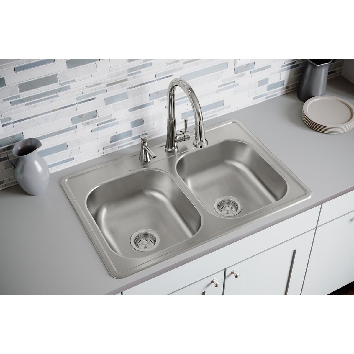 Stainless steel double bowl drop-in sink with two faucet holes and chrome pull-down faucet installed in white countertop.