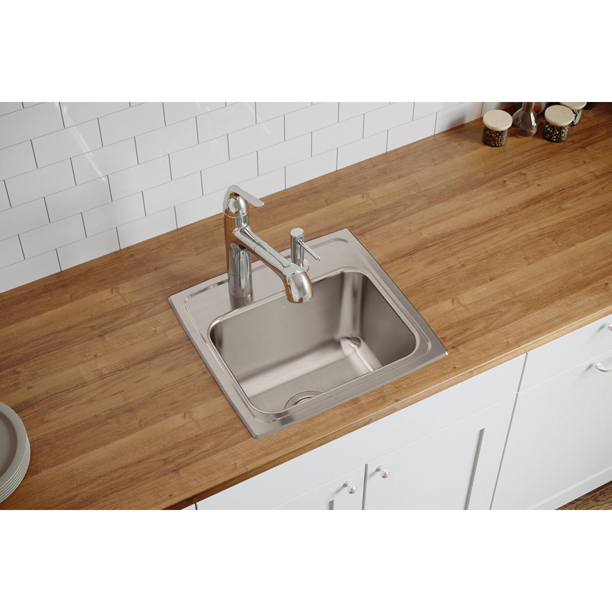 Stainless steel drop-in sink with single bowl and two faucet holes, installed in wooden countertop with chrome faucet.