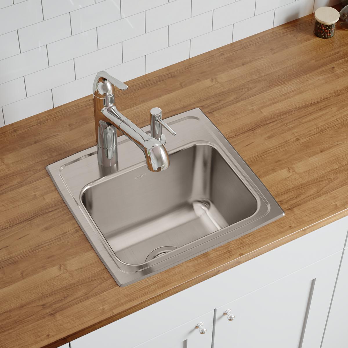Stainless steel single bowl drop-in sink with two faucet holes installed on wood countertop with chrome faucet.