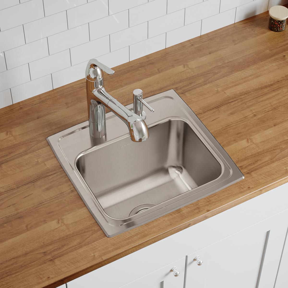 Stainless steel single bowl drop-in sink with three faucet holes installed in wood countertop with chrome faucet and sprayer.