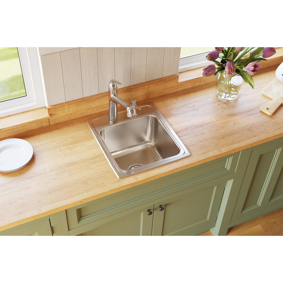 Stainless steel single bowl drop-in sink with two faucet holes installed in wooden countertop.