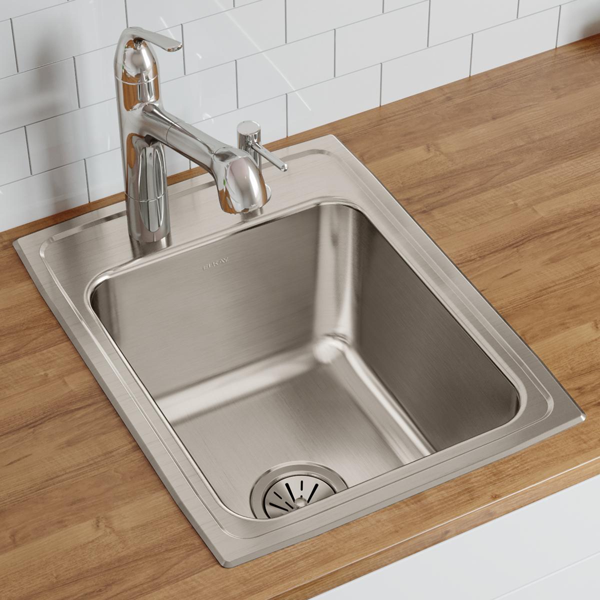 Stainless steel single bowl drop-in sink with three faucet holes mounted in wood countertop with chrome faucet.