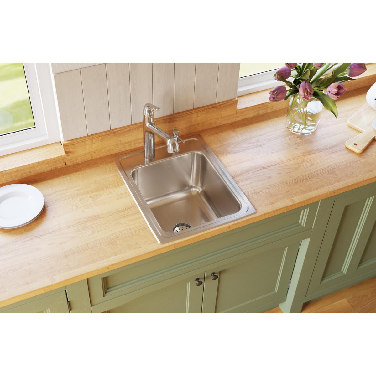 Stainless steel drop-in sink with single bowl and two holes mounted in wood countertop with chrome faucet.