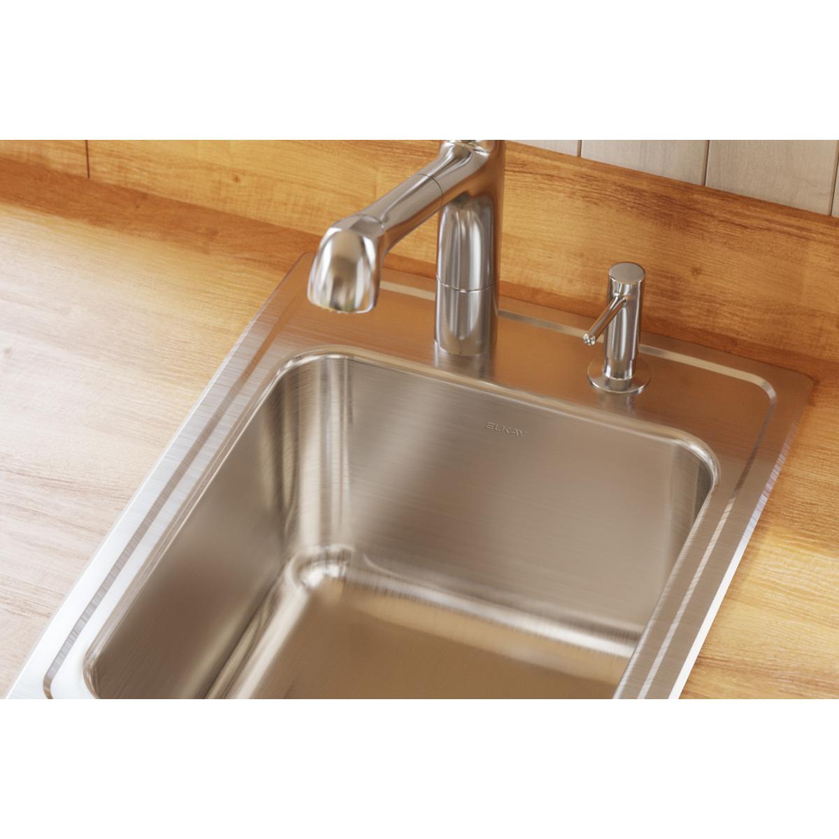 Stainless steel single bowl drop-in sink with faucet and soap dispenser installed in wood countertop.