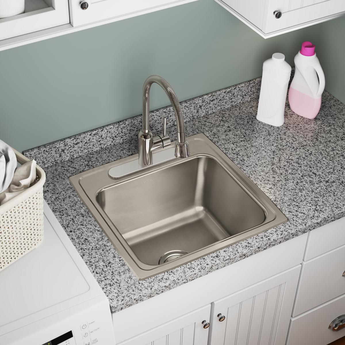 Stainless steel drop-in laundry sink with single bowl and faucet installed in granite countertop with white cabinets below.