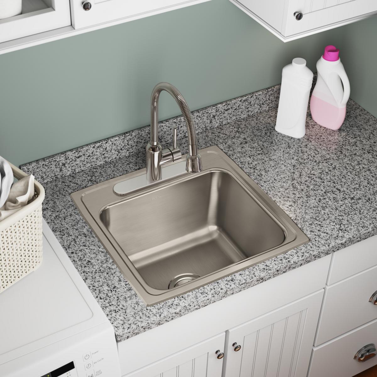 Stainless steel drop-in laundry sink with single bowl and two faucet holes installed in granite countertop.