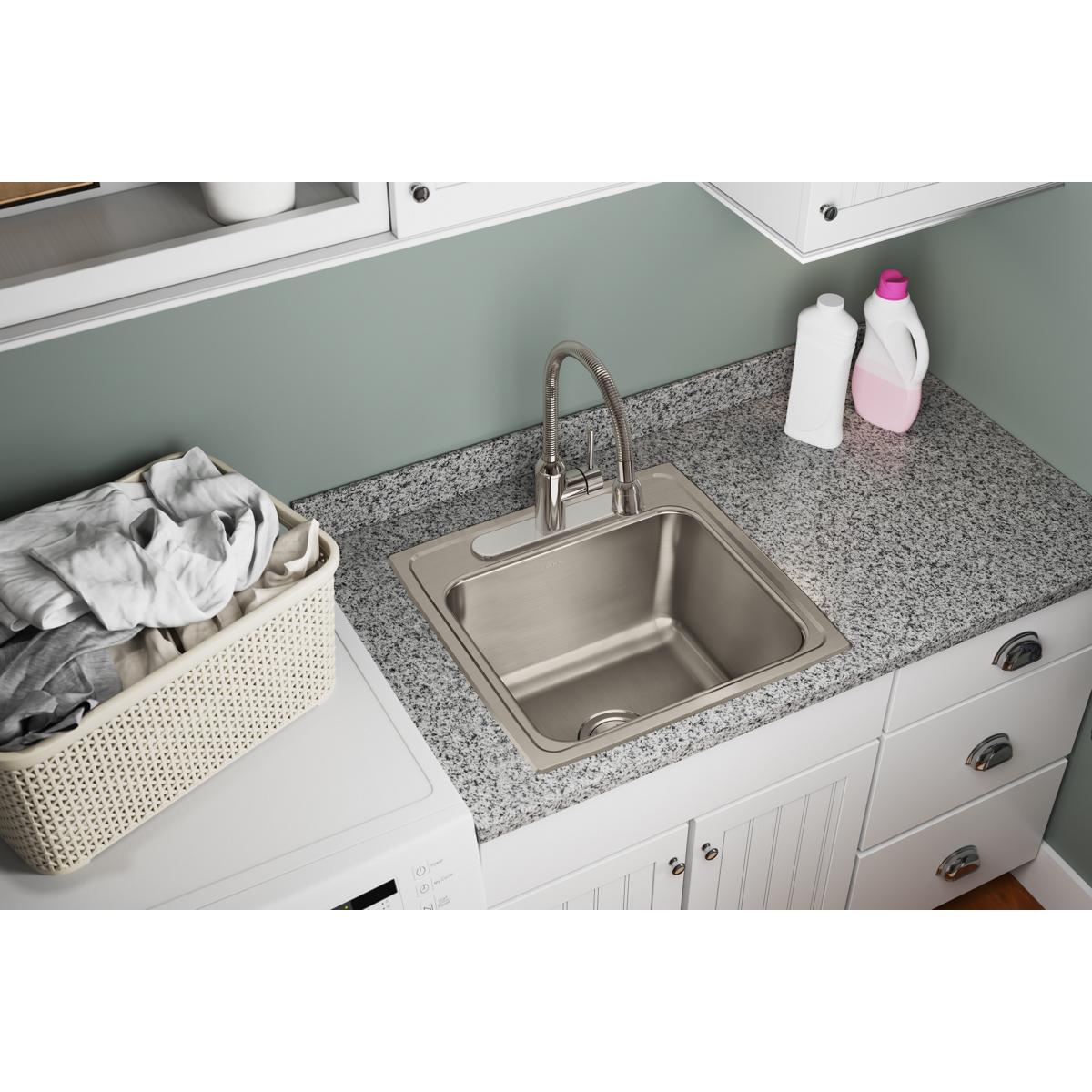 Stainless steel single bowl drop-in laundry sink installed in granite countertop with faucet and cleaning supplies nearby.