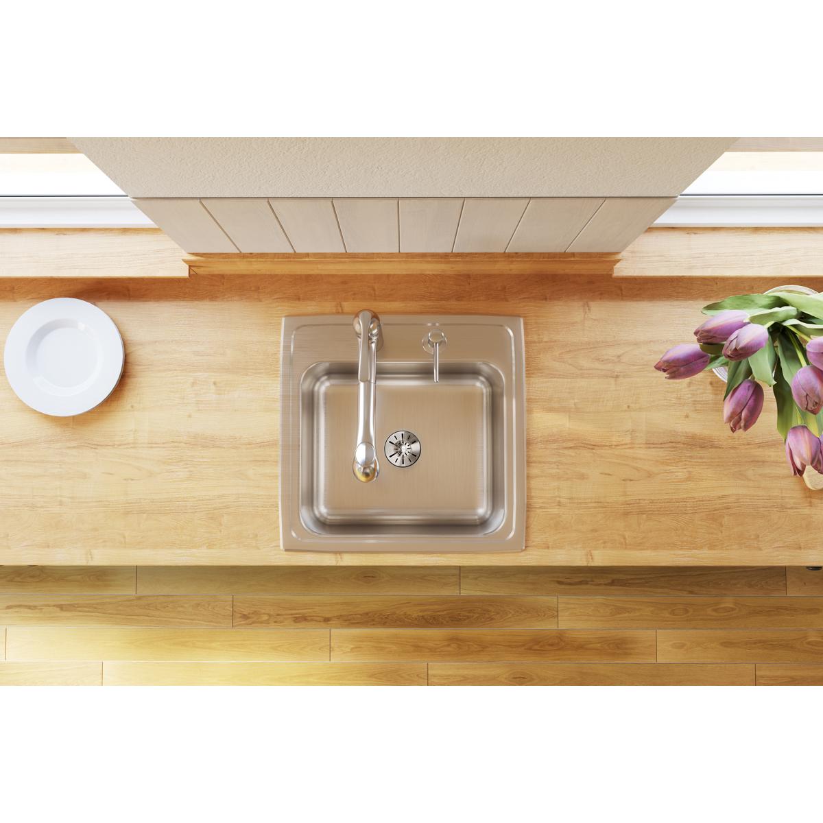 Stainless steel single bowl drop-in laundry sink with drain installed in wooden countertop.