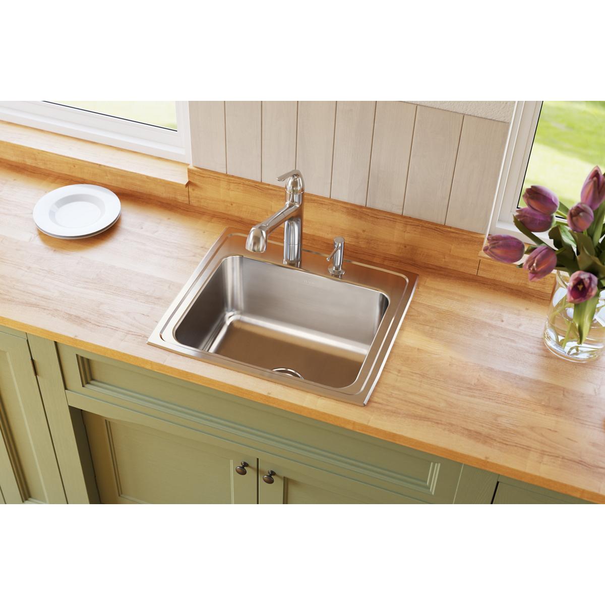 Stainless steel drop-in sink with single bowl and two faucet holes installed in wood countertop with chrome faucet.