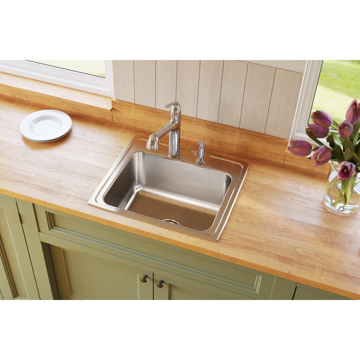 Stainless steel drop-in sink with single bowl and chrome faucet installed in wood countertop with green cabinetry.