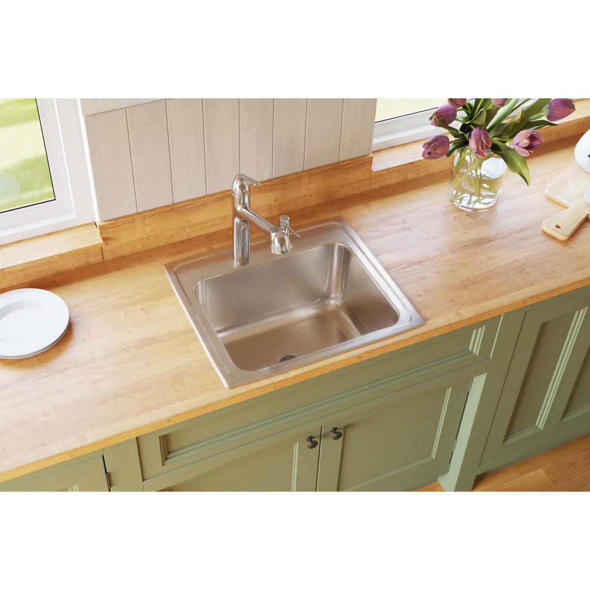 Stainless steel single bowl drop-in sink installed in wood countertop with chrome faucet and green cabinet base.