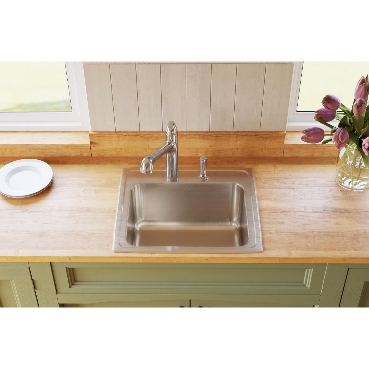 Stainless steel single bowl drop-in sink with two faucet holes installed in wooden countertop with chrome faucet.