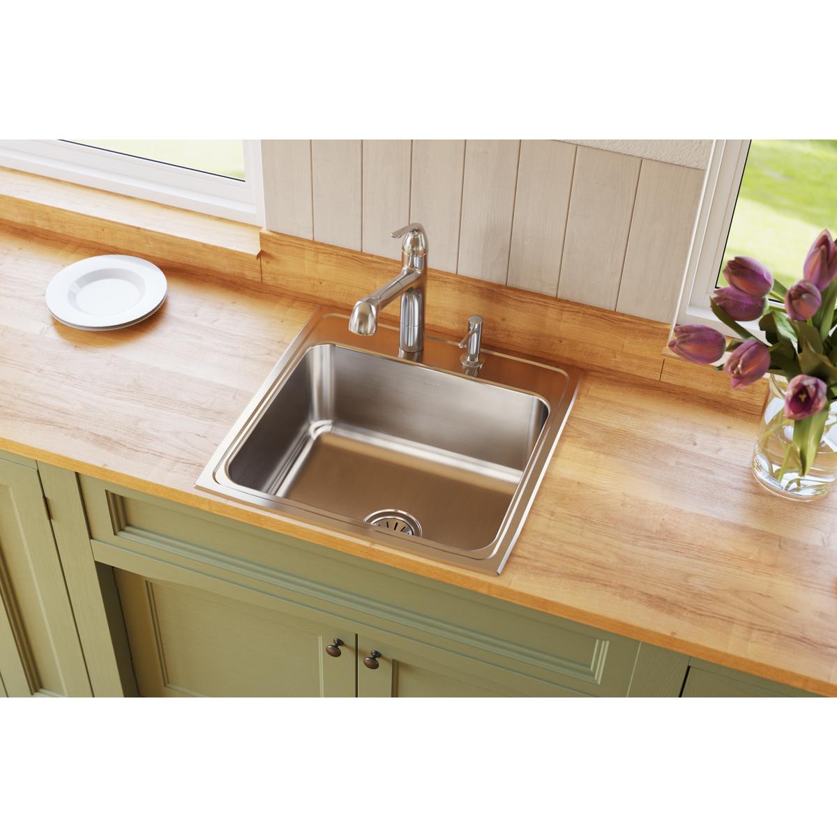 Stainless steel drop-in sink with single bowl and faucet installed in wooden countertop above green cabinets.