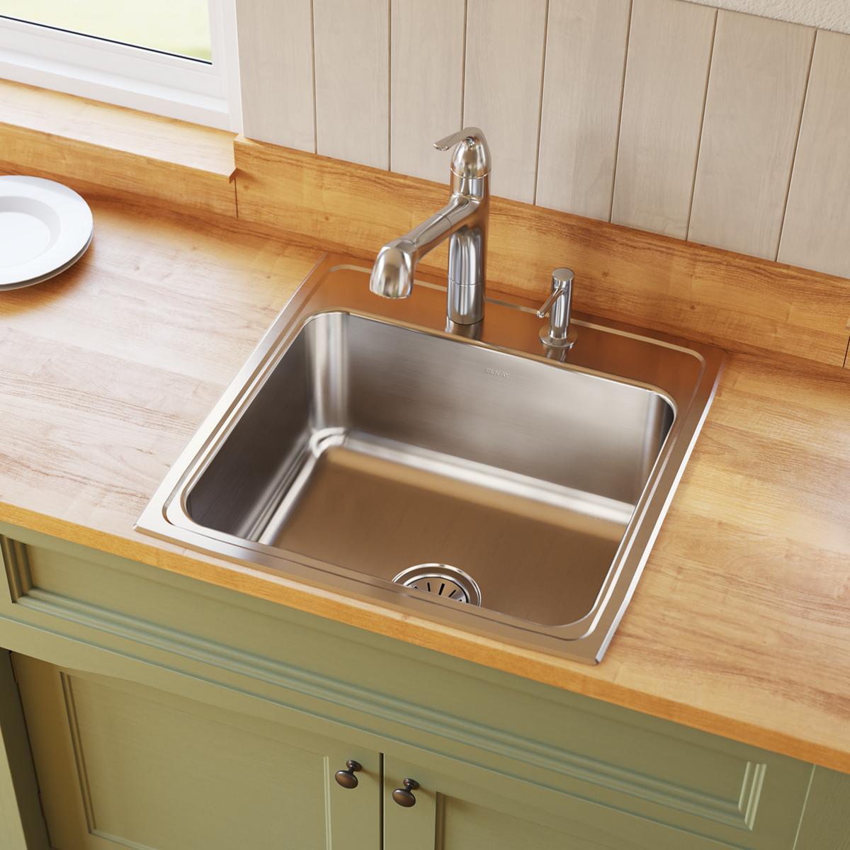 Stainless steel drop-in kitchen sink with single bowl, chrome faucet and sprayer mounted on wooden countertop.