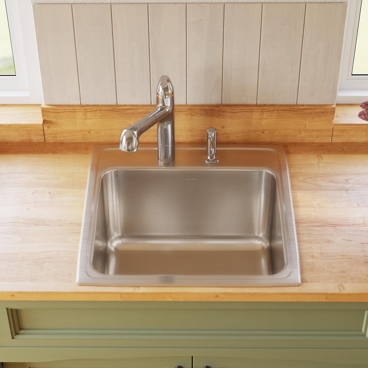 Stainless steel single bowl drop-in sink with chrome faucet and soap dispenser installed in wooden countertop.