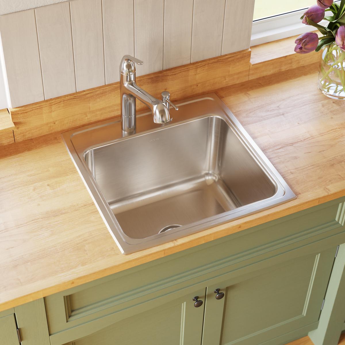 Stainless steel single bowl drop-in sink installed in wood countertop with chrome faucet and soap dispenser.