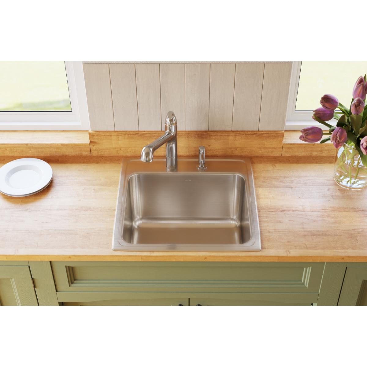 Stainless steel single bowl drop-in sink with faucet mounted on wood countertop in kitchen.