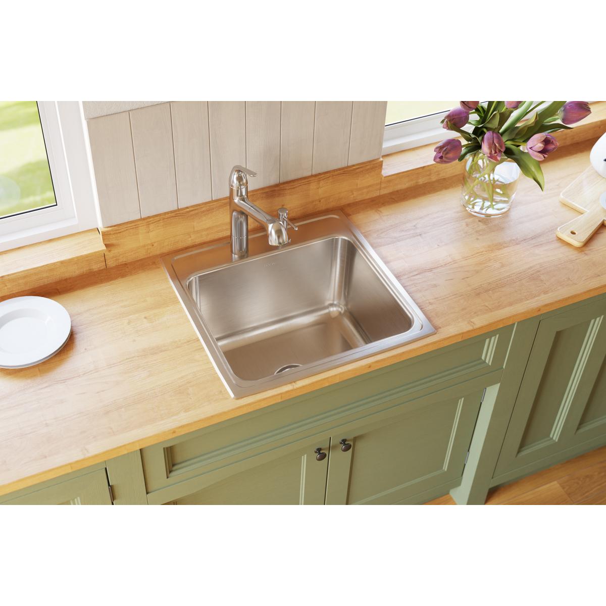 Stainless steel single bowl drop-in sink with two faucet holes installed in wood countertop with chrome faucet.