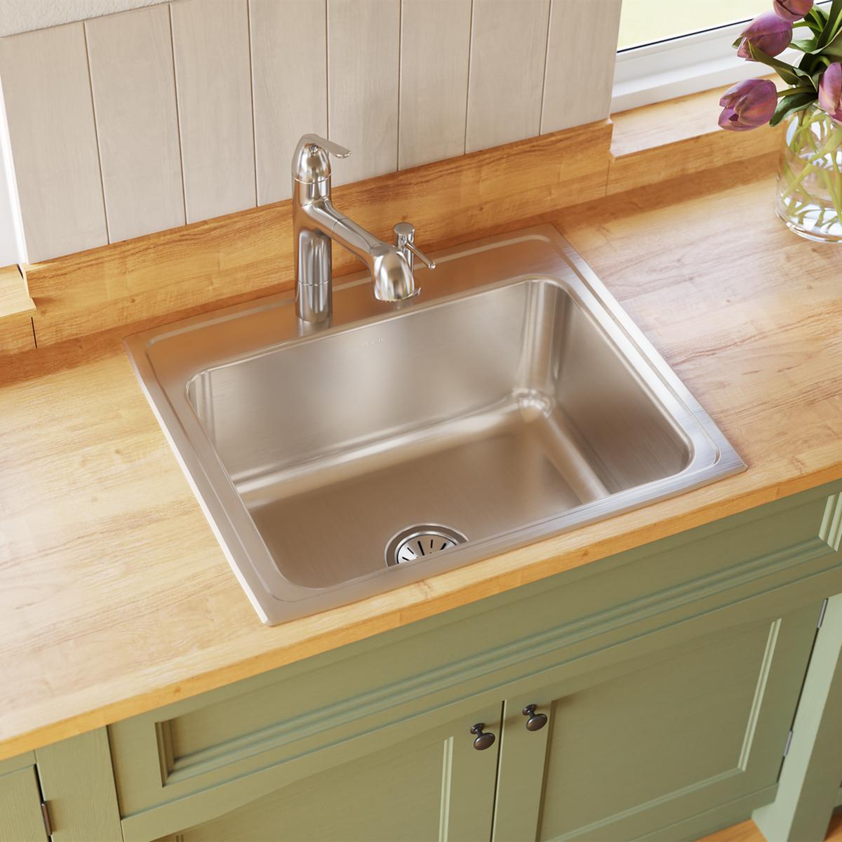 Stainless steel drop-in kitchen sink with single bowl and drain, installed in wooden countertop with chrome faucet.