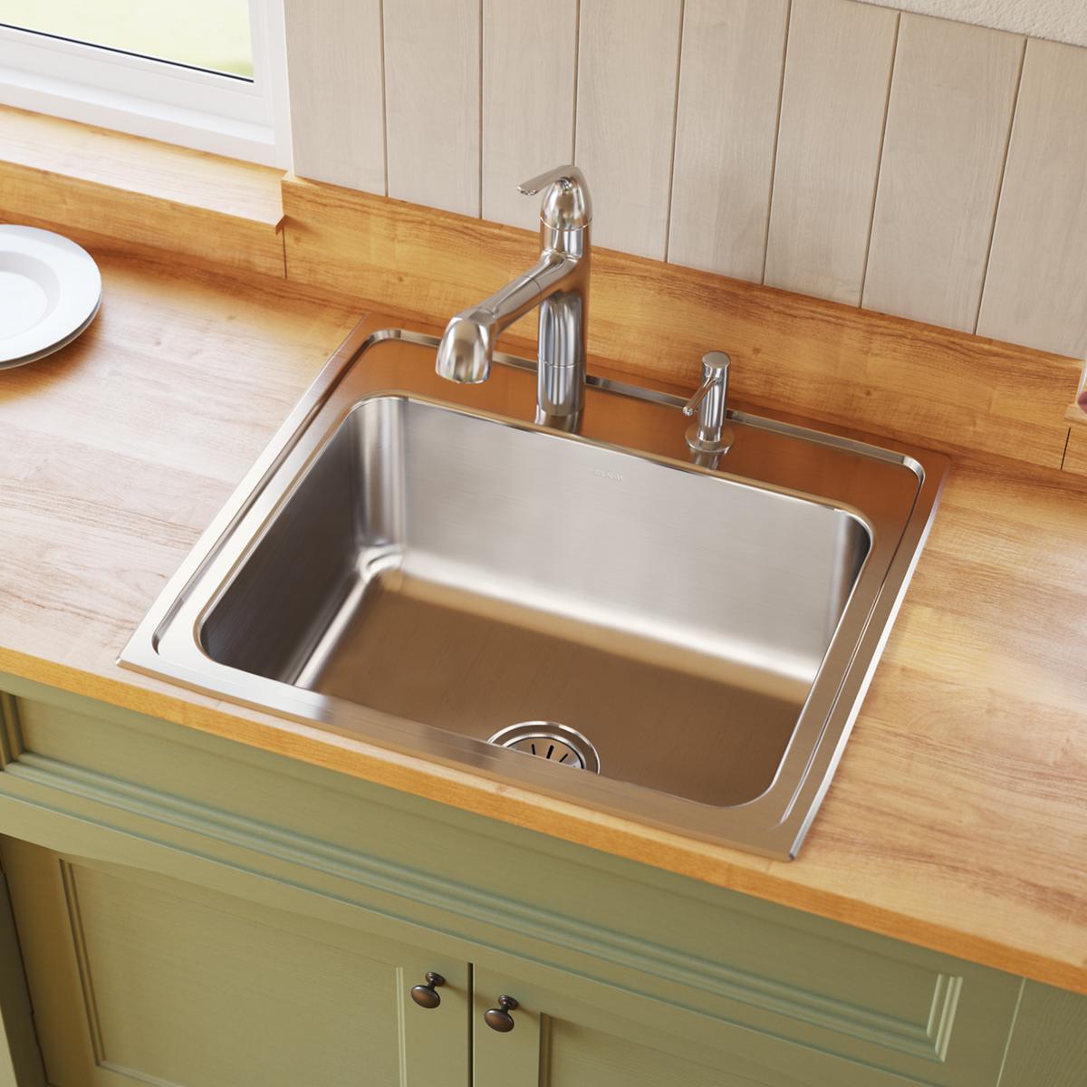 Stainless steel single bowl drop-in sink with two faucet holes and chrome faucet installed on wooden countertop.