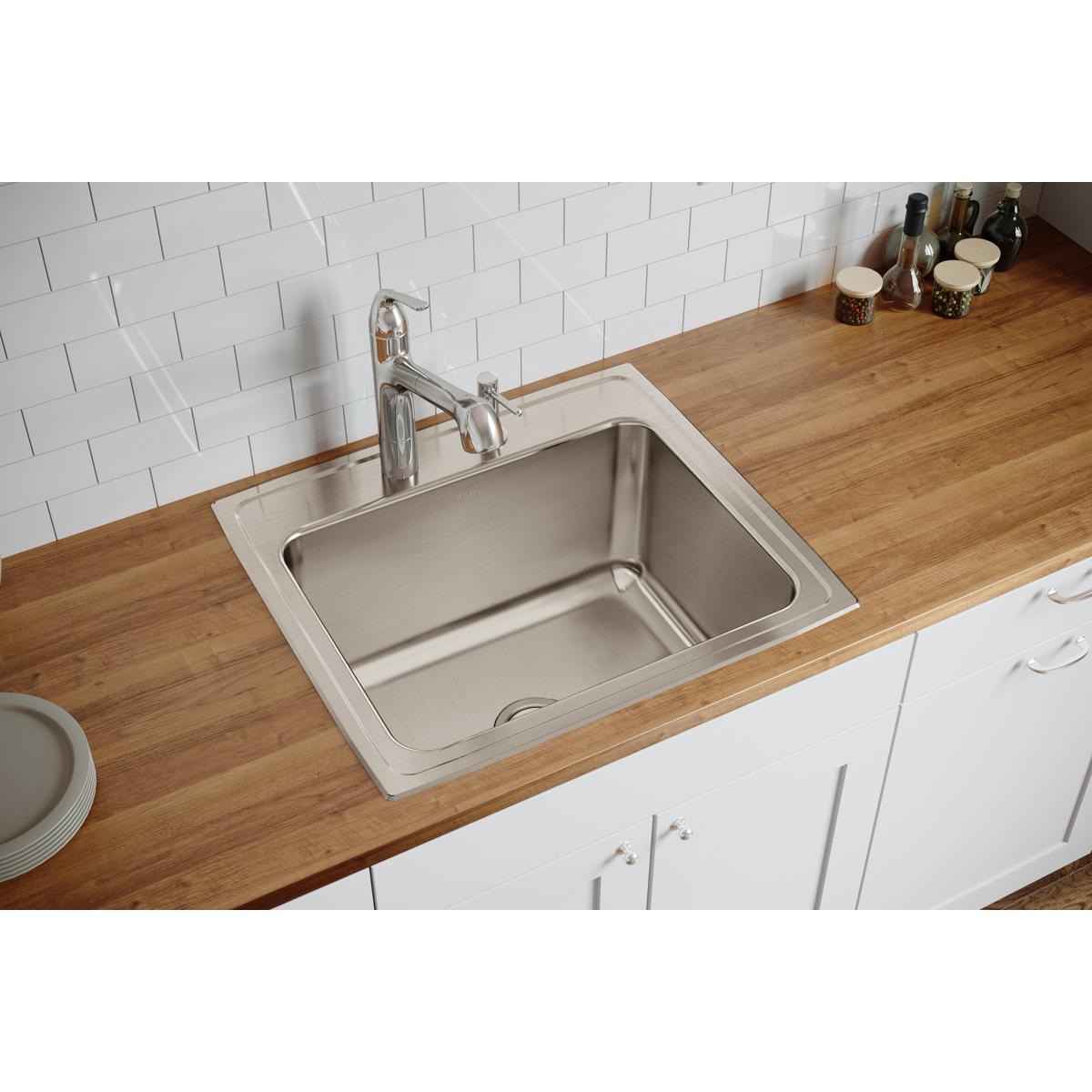 Stainless steel drop-in sink with single bowl mounted in wood countertop, chrome faucet, white subway tile backsplash visible