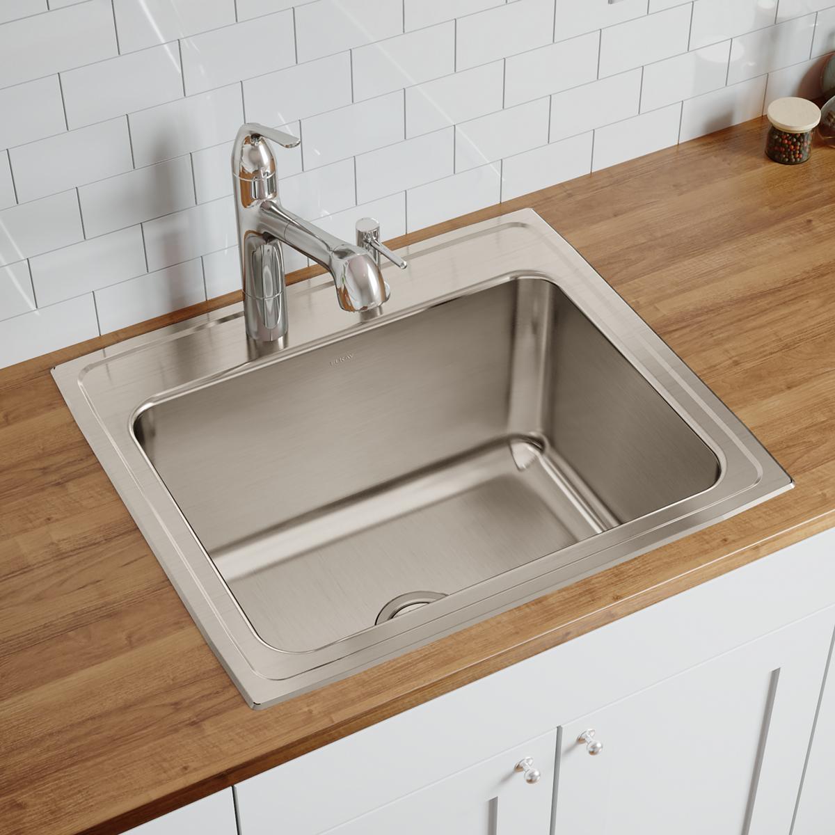 Stainless steel drop-in sink with single bowl installed in wood countertop, chrome faucet, white subway tile backsplash.