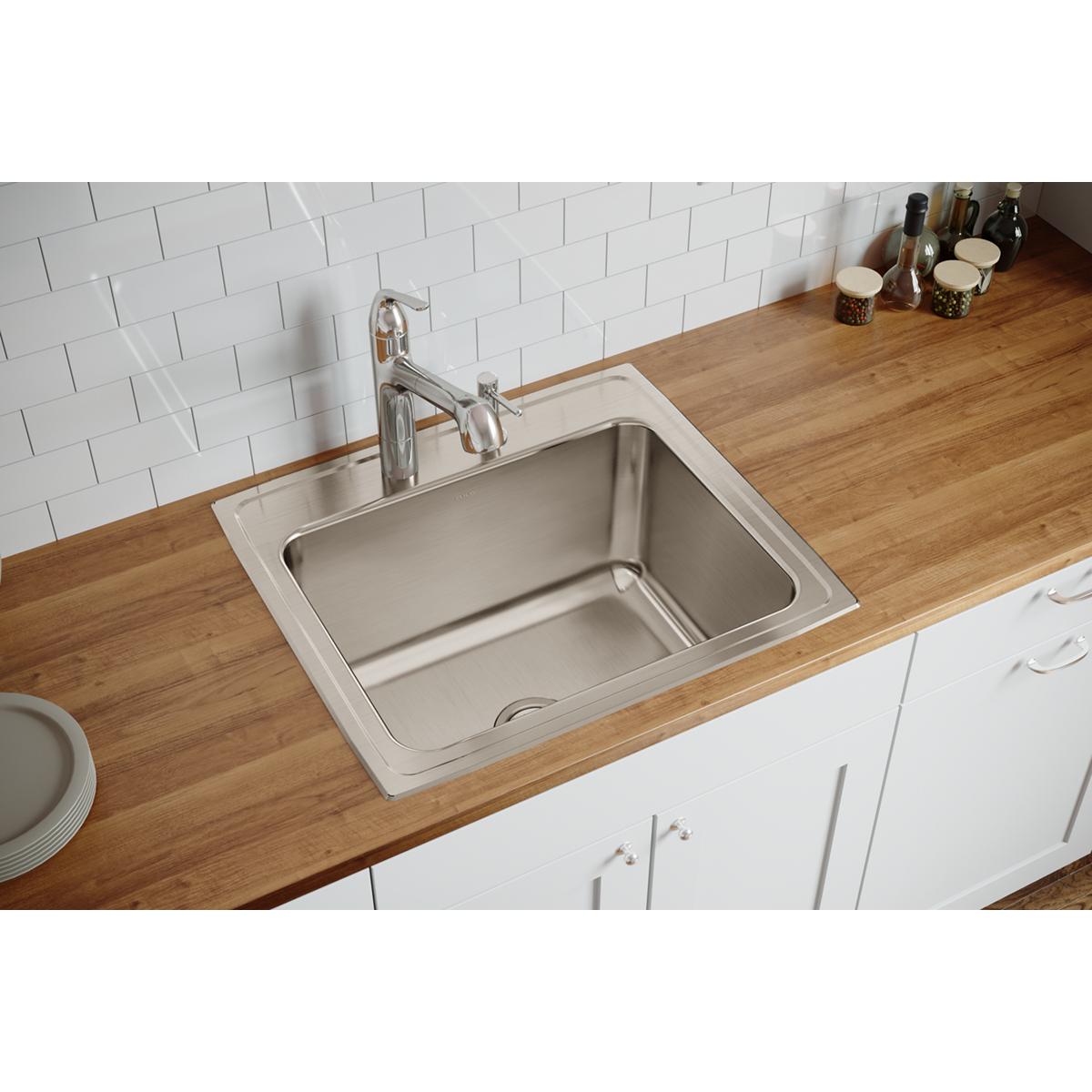 Stainless steel single bowl drop-in sink with two faucet holes installed in wood countertop with white subway tile backsplash