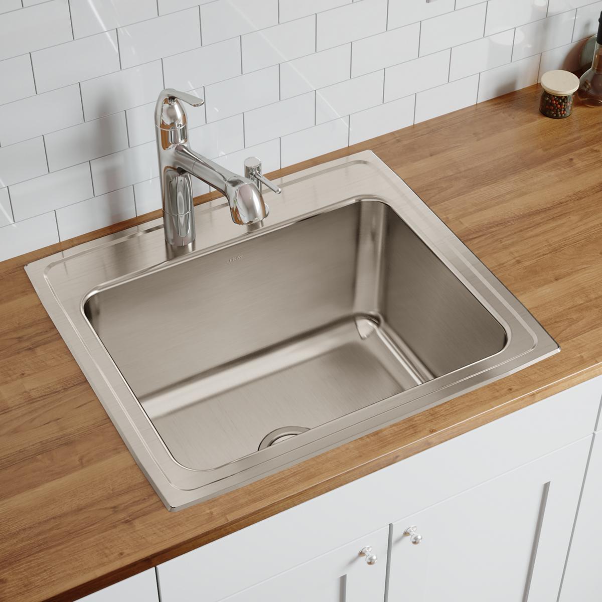Stainless steel drop-in sink with single bowl and four holes mounted in wooden countertop with chrome faucet and white subway