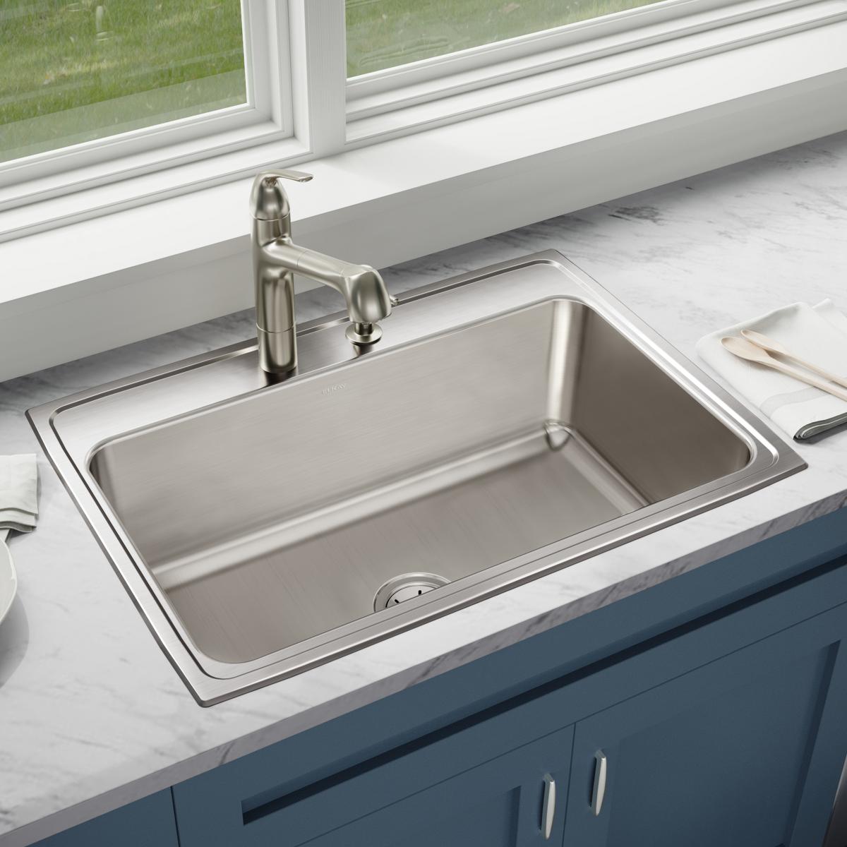 Stainless steel drop-in sink with single bowl and three holes, installed in white marble countertop with faucet.