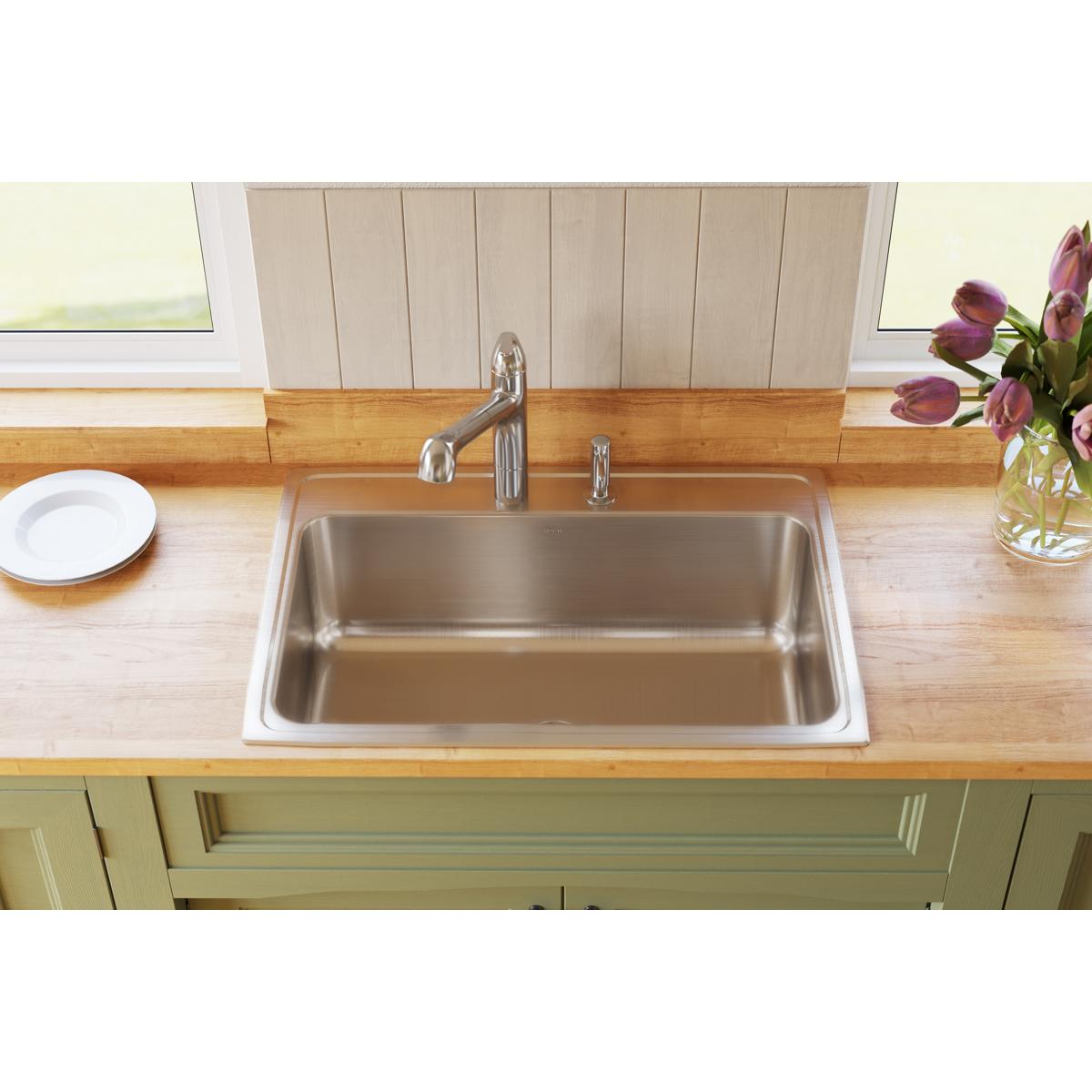 Stainless steel rectangular drop-in sink with single bowl, two faucet holes, and chrome faucet installed in wooden countertop