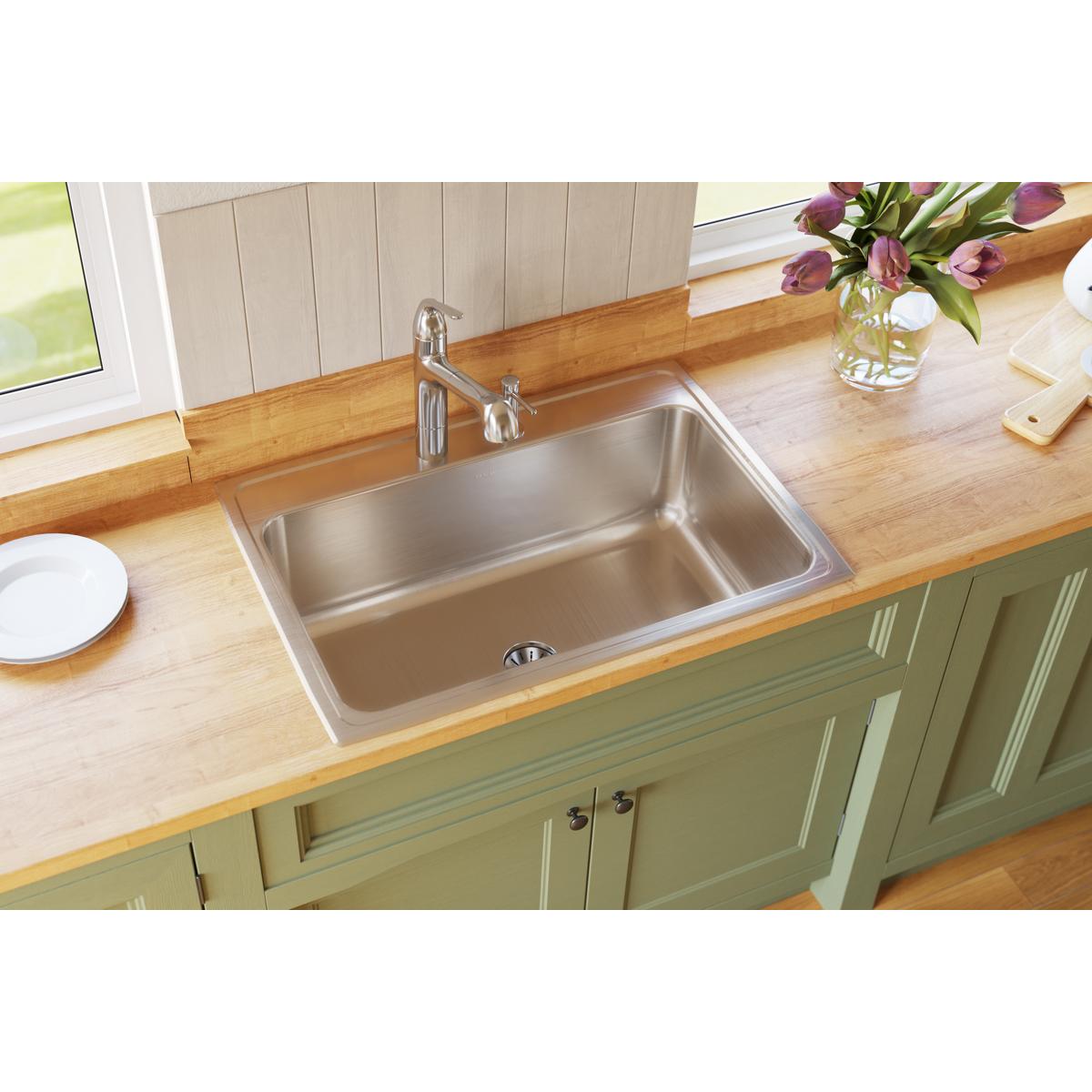 Stainless steel single bowl drop-in sink installed in wooden countertop with chrome faucet and green cabinet base.