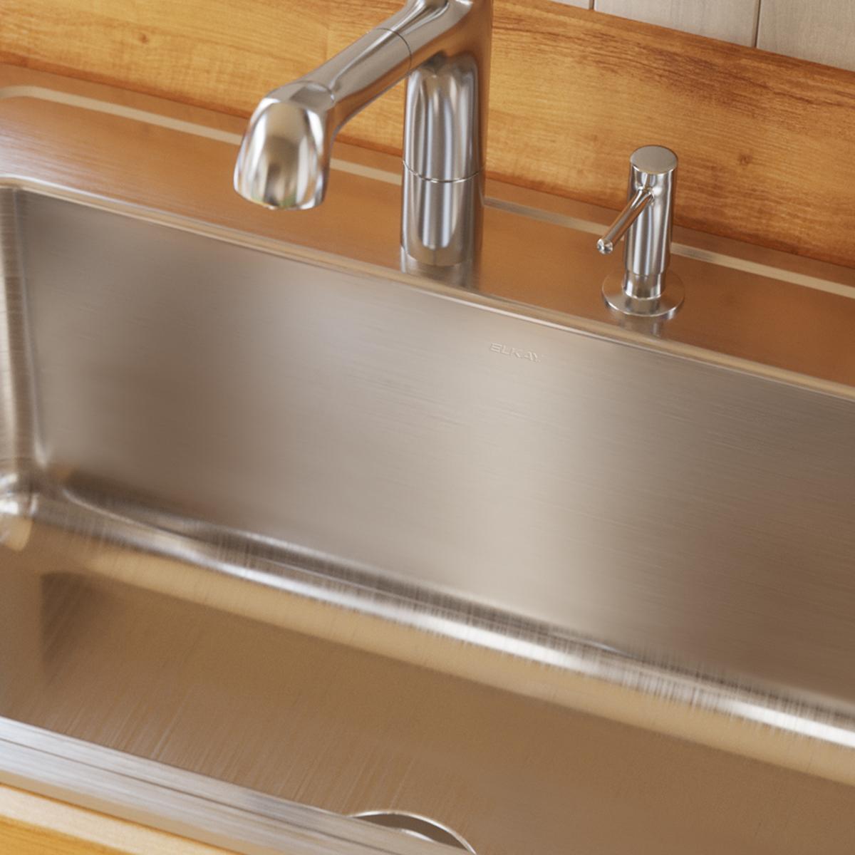 Stainless steel single bowl drop-in sink with brushed finish installed in wooden countertop, shown with faucet and spray atta