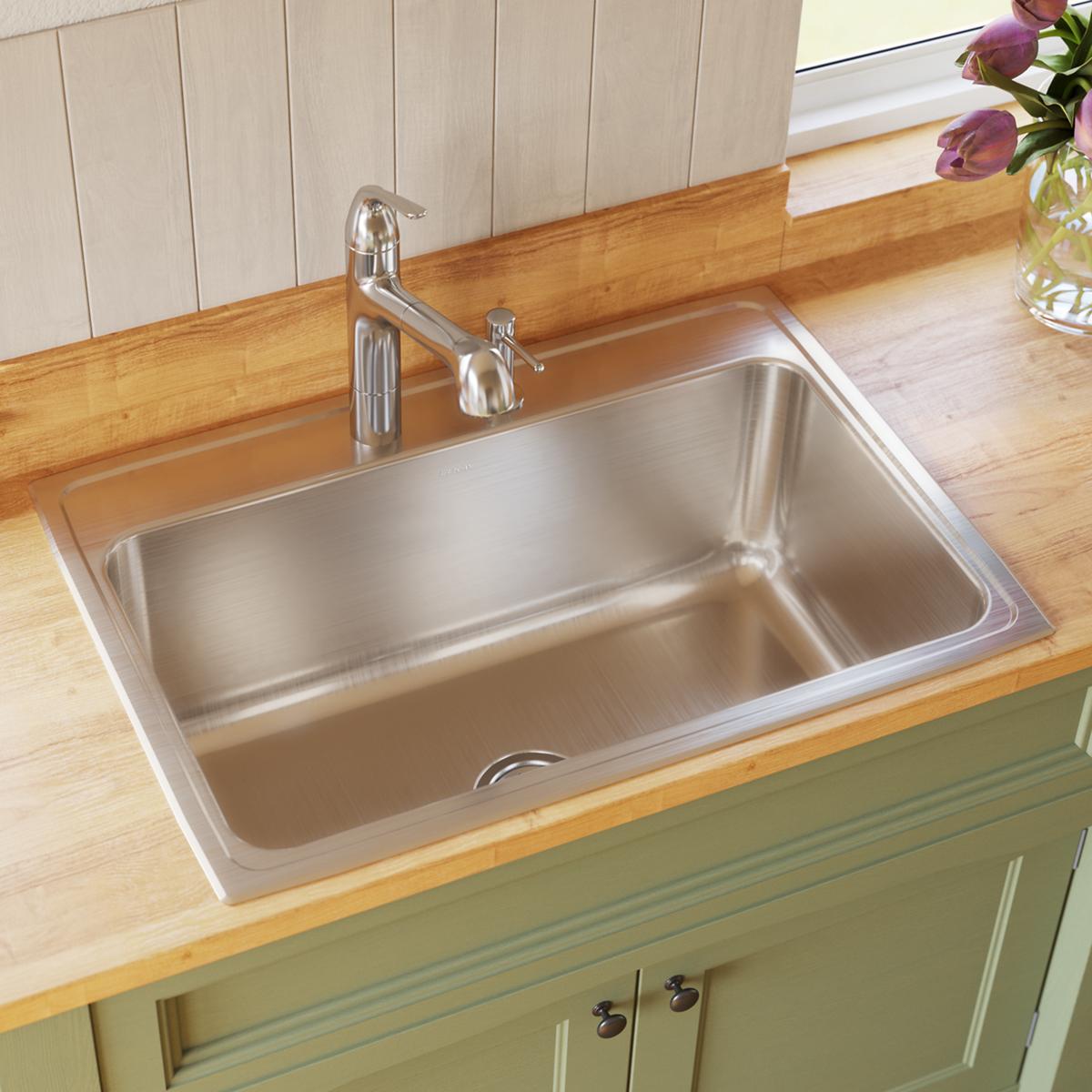 Stainless steel single bowl drop-in sink with one faucet hole, installed in wooden countertop with chrome faucet.