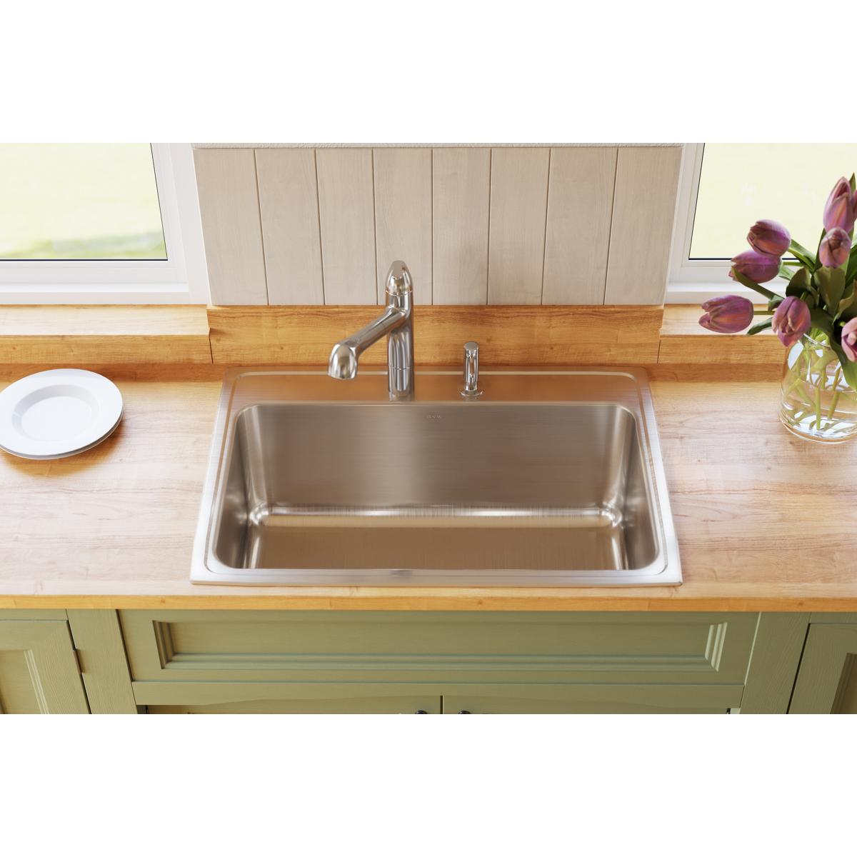 Stainless steel drop-in sink with single bowl and two faucet holes installed in wooden countertop.