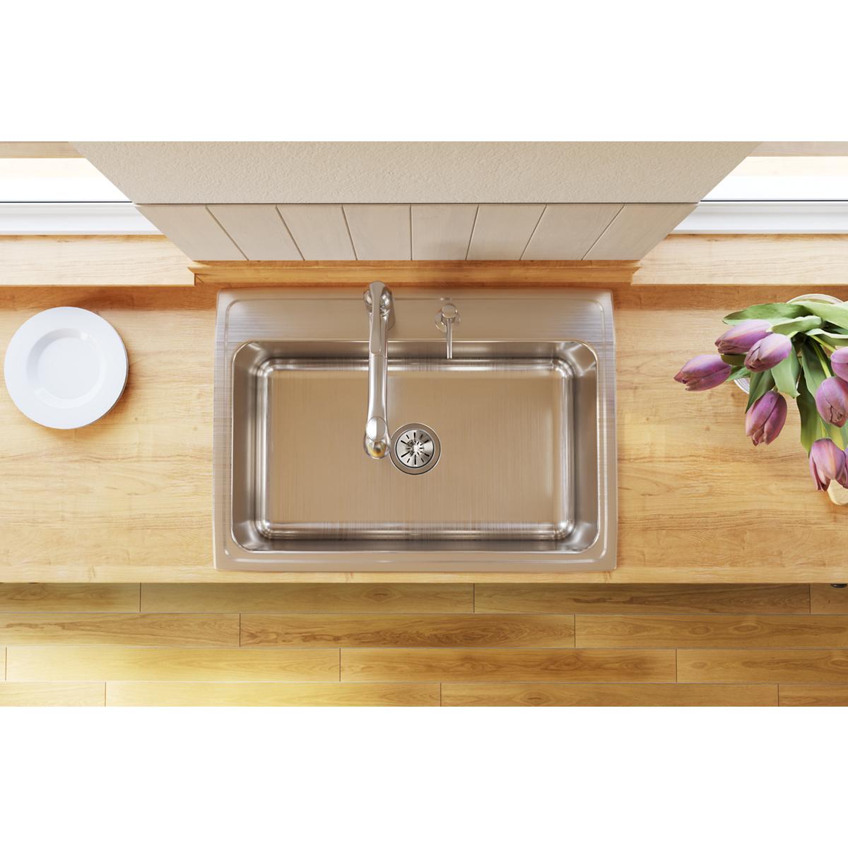Stainless steel single bowl drop-in sink with two faucet holes installed in wood countertop.
