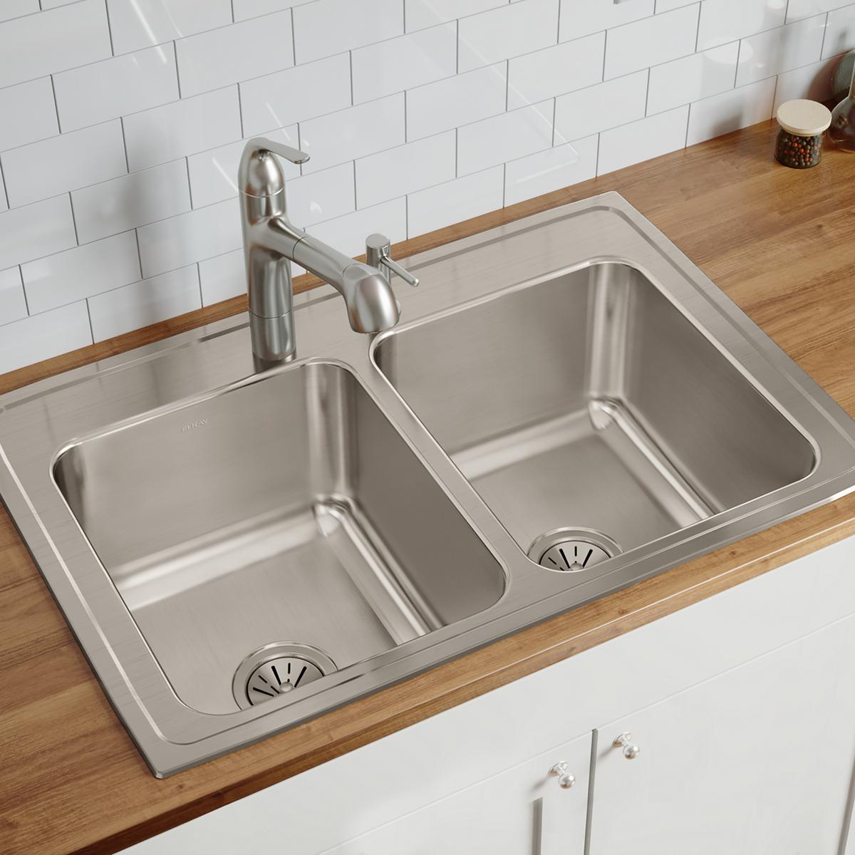 Stainless steel double bowl drop-in sink with two equal-sized basins, drains, and three faucet holes installed on wood counte