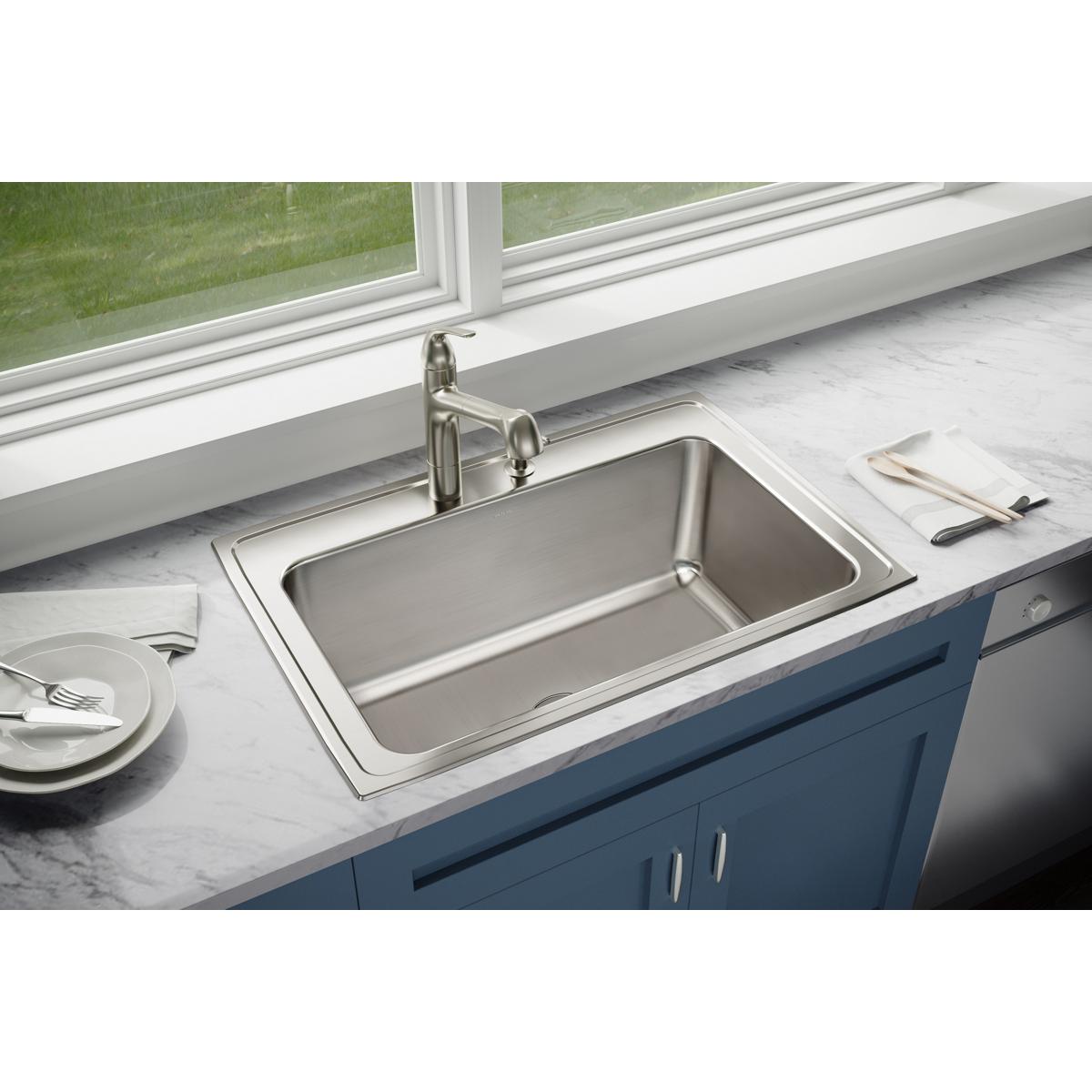 Stainless steel drop-in sink with single bowl and chrome faucet installed in countertop next to window.